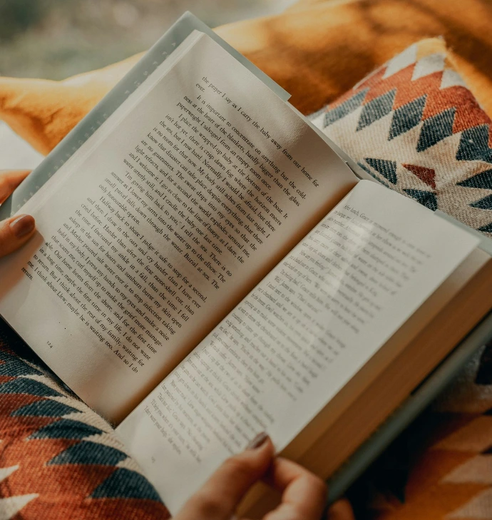 person reading book on brown and beige textile